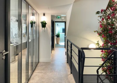 Le couloir de cette agence bancaire de La Crau mène vers le bureau de la direction et donne à voir la salle des collaborateur et un escalier à double sens. La transparence des cloisons modulaires montre que l'architecture a été pensé en terme de luminosité, de transparence et de matérialité. Le matériaux, choisis pour leur durabilité et leur éco-responsabilité.