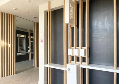 Le hall de l'agence bancaire de Grasse Saint-Jacques conçue par l'agence d'architecture ESPERLUETTE STUDIO est composée d'éléments naturels comme le sol et le bois mais aussi d'une tôle laminée à chaud qui recouvre les murs. Les miroirs servent à agrandir l'espace des distributeurs, astuce d'architecte.