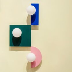Luminaires en trois versions rond type boule de la marque SWEDISH NINJA, sur un fond vert foncé, un fond bleu électrique et un fond rose pâle. Ces appliques sont accrochées à un mur teinte jaune.